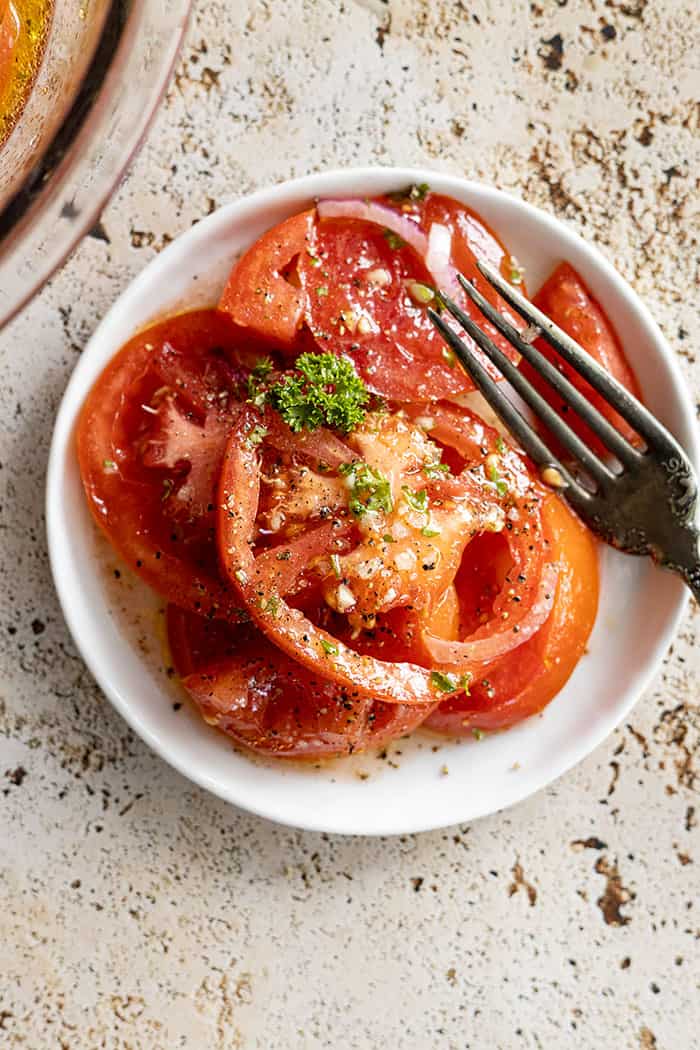 overhead closeup: marinated tomatoes on a white plate with a fork off to the side