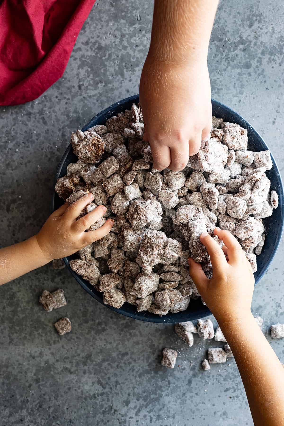 Overhead view of children's hands reaching into the bowl to grab some puppy chow. 