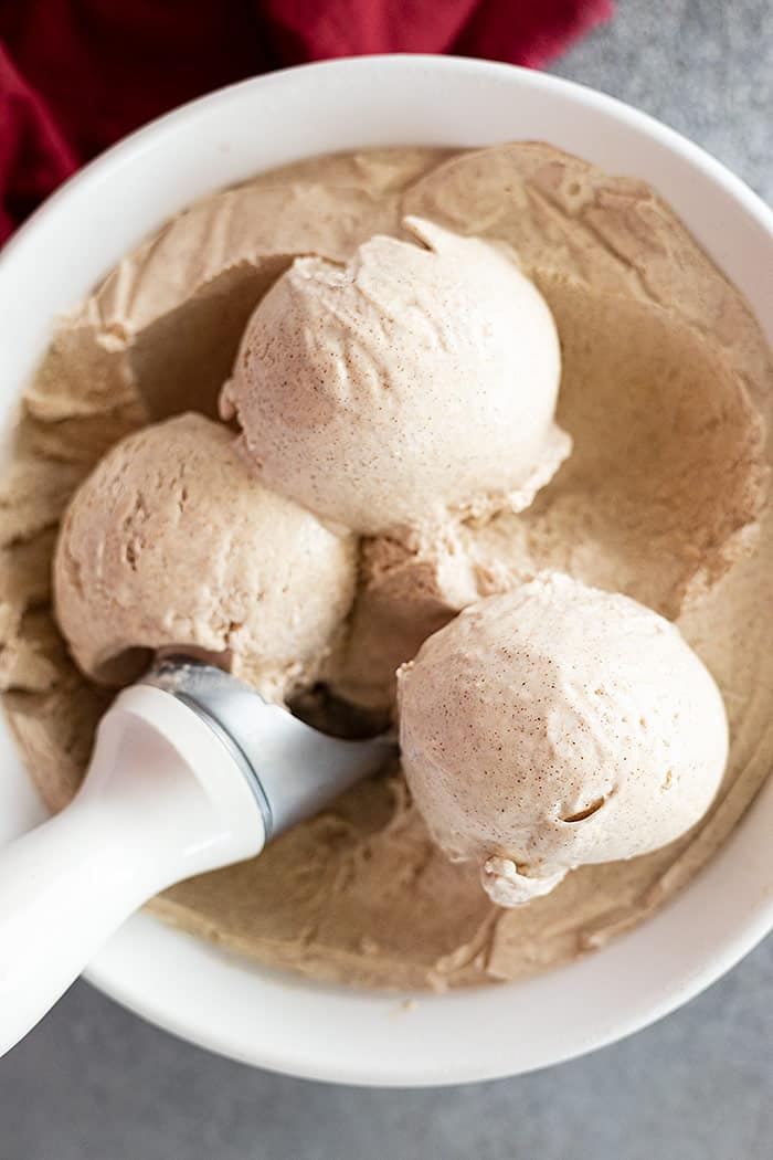 Three scoops of ice cream sitting on top of the rest of the ice cream in the container. 