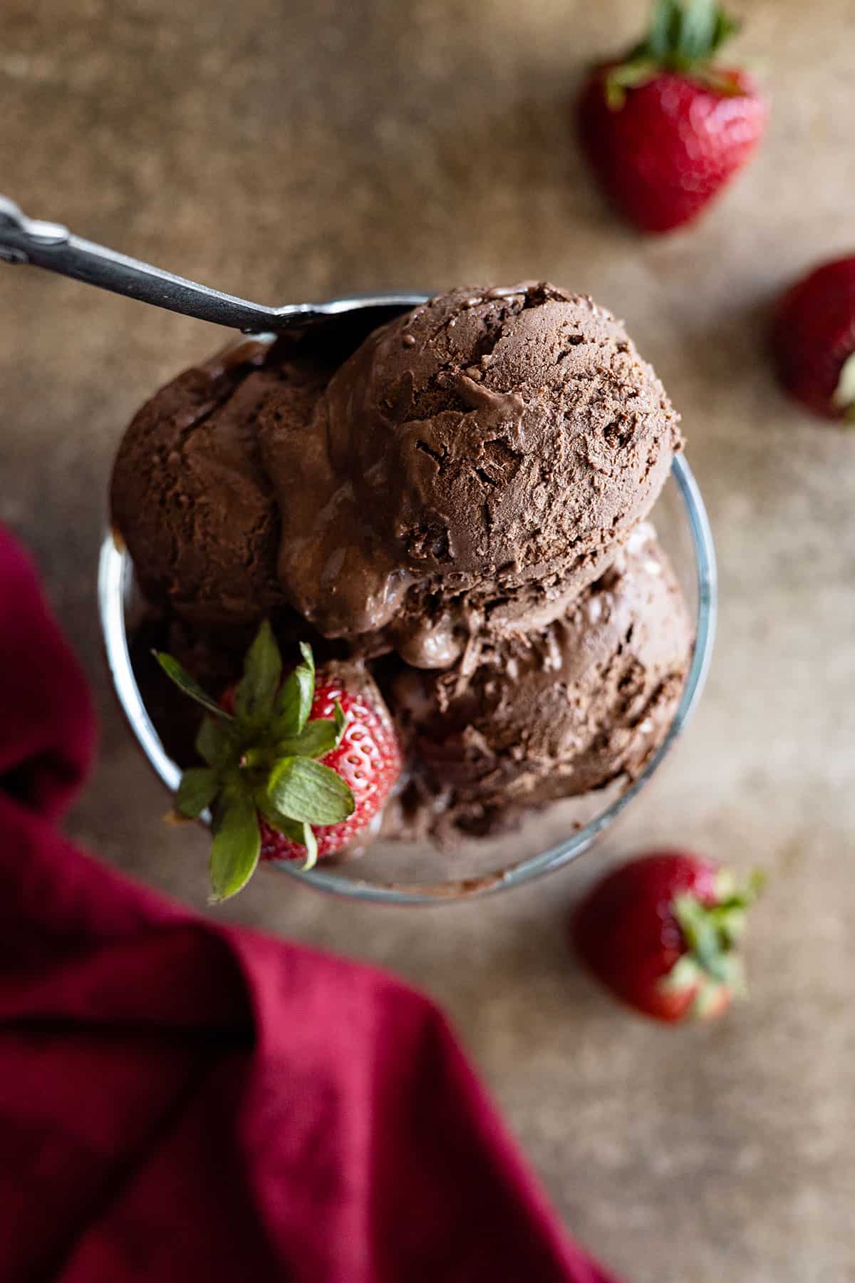 Overhead view of scoops of ice cream in a glass bowl with strawberries to the side.
