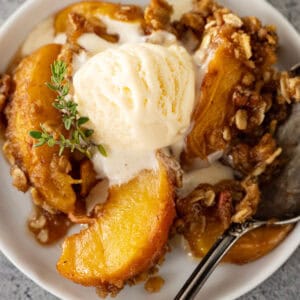 Overhead view of peach crisp on a white plate with ice cream slowly melting into the crisp.