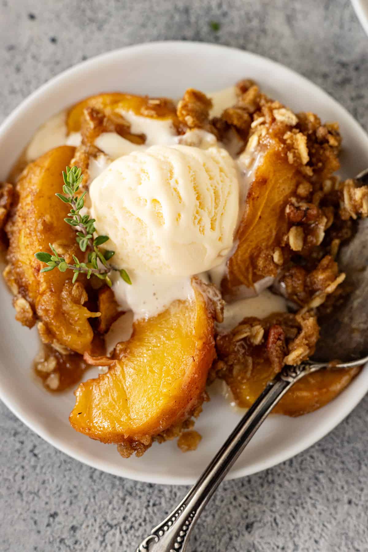 Overhead view of peach crisp on a white plate with ice cream slowly melting into the crisp.