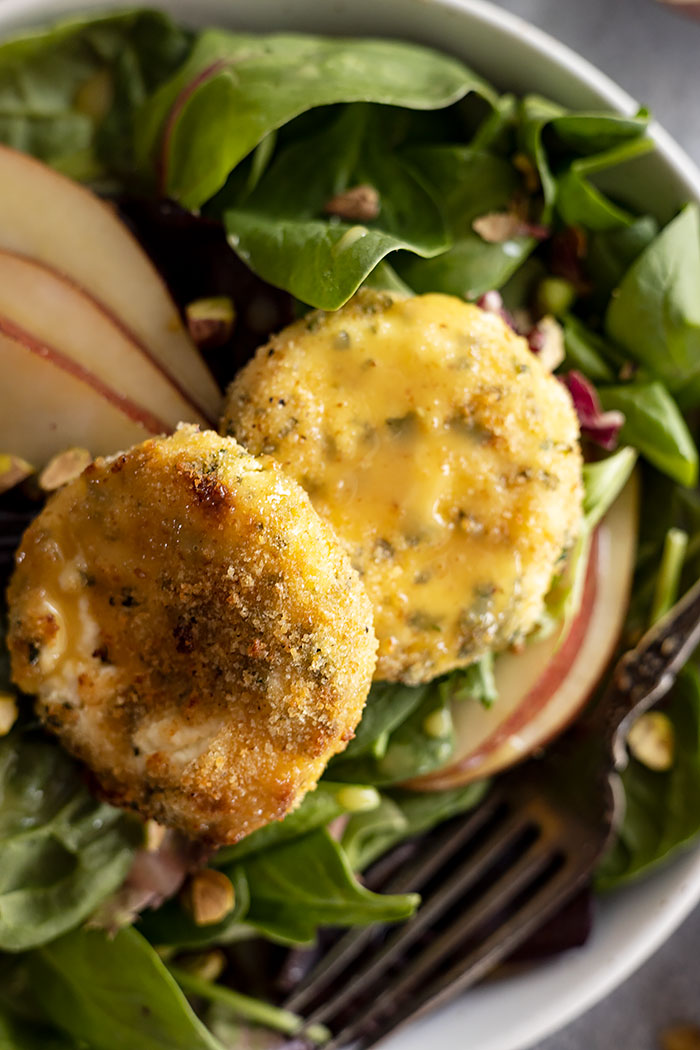 Close up of salad with goat cheese, dressing drizzled, and pear slices.
