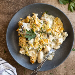 Overhead view of poppy seed chicken casserole on a dark blue plate with a fork. Garnished with fresh parsley and black pepper.