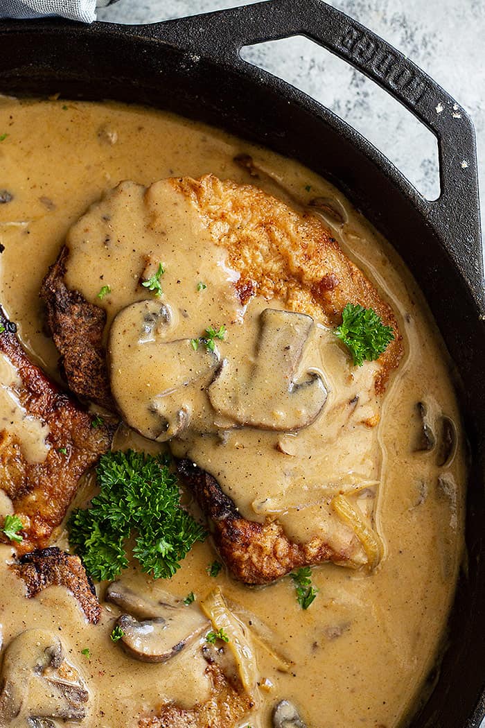Top down view of pork chops in mushroom gravy in cast iron skillet.
