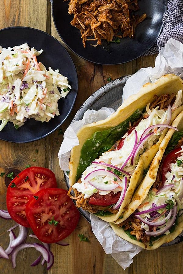 overhead: two black plates with coleslaw and pulled pork next to plate of pork gyros