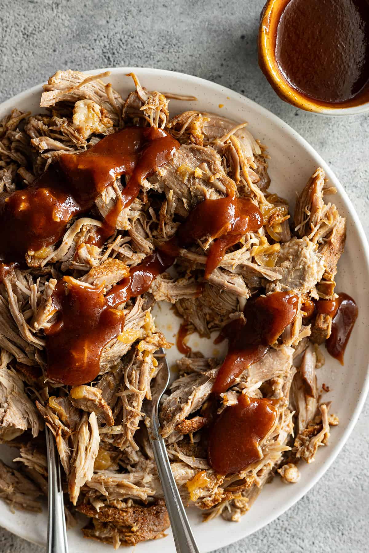 Overhead view of pork on a white plate drizzled with bbq sauce. 