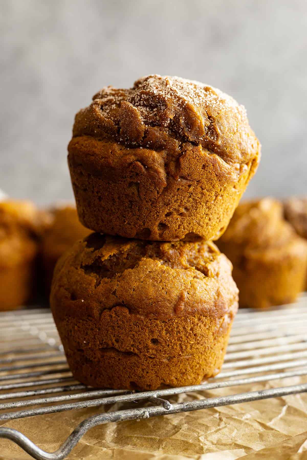 Two muffins stacked on top of each other on top of a cooling rack. More muffins in the background. 
