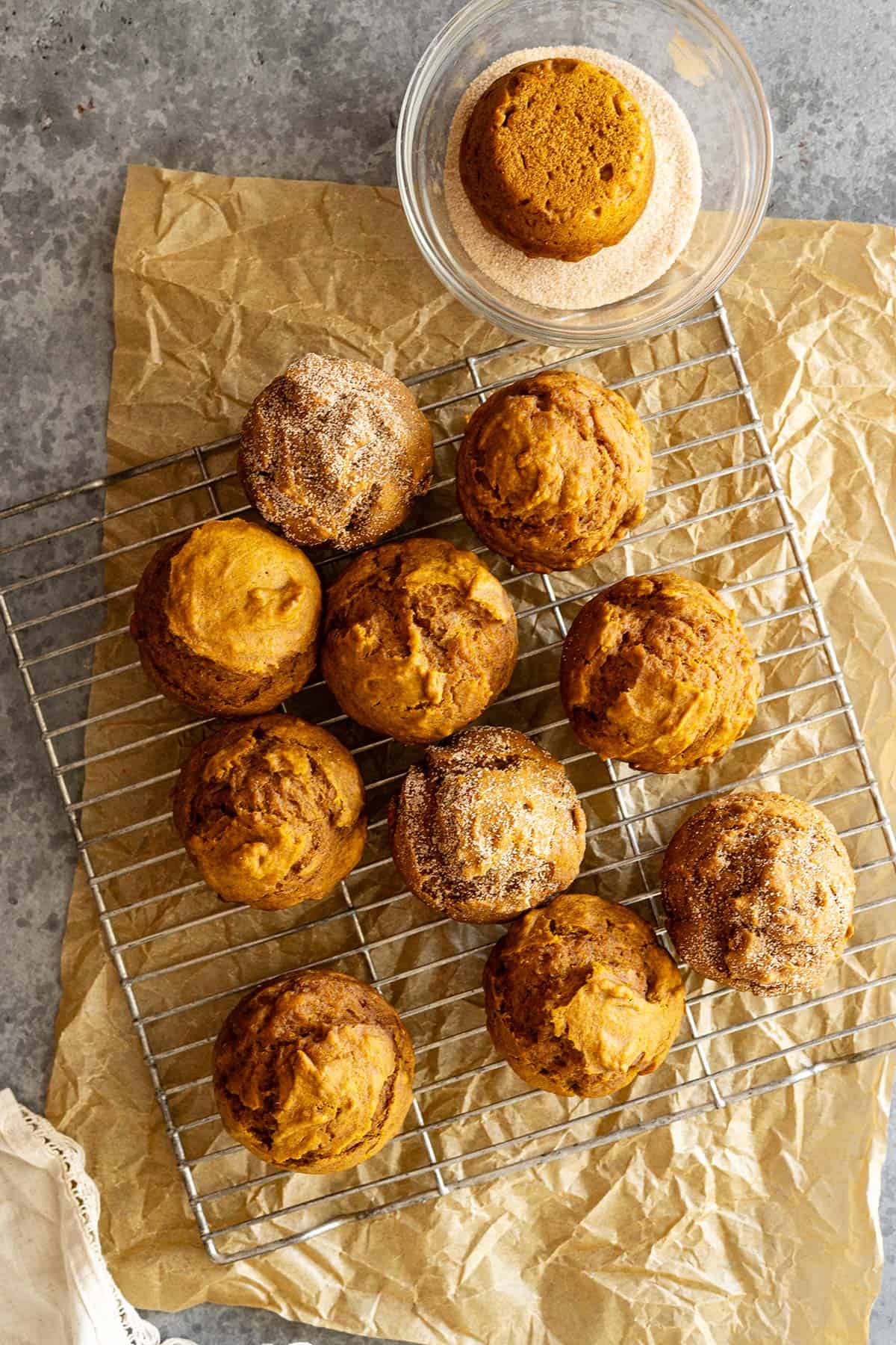 Overhead view of pumpkin muffins on a cooling rack. Some topped with a dusting of cinnamon sugar. 