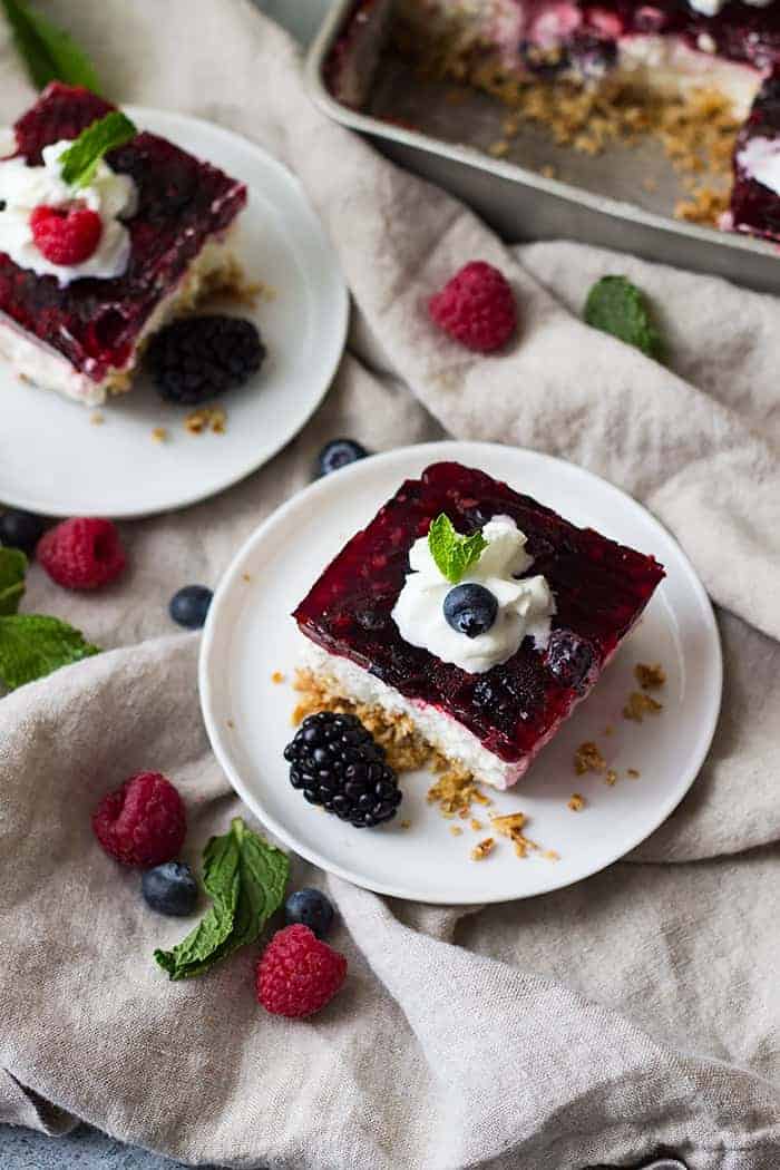 overhead: a slice of raspberry pretzel salad on a white plate with mixed berries and whipped cream on top