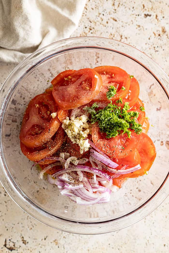 overhead closeup: all the ingredients for this recipe for marinated tomatoes in a bowl ready to be mixed 