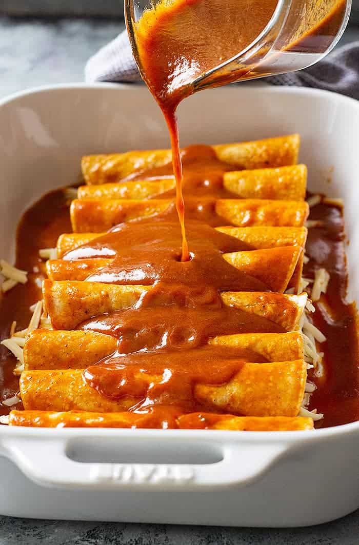 Red enchilada sauce being poured over enchiladas.