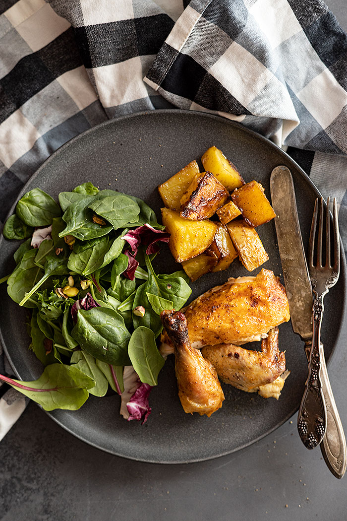 Overhead view of cornish hen pieces on a plate with roasted potatoes and a green salad. 