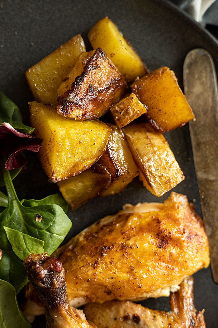 Close up of roasted potatoes with the cornish hen on a plate. 