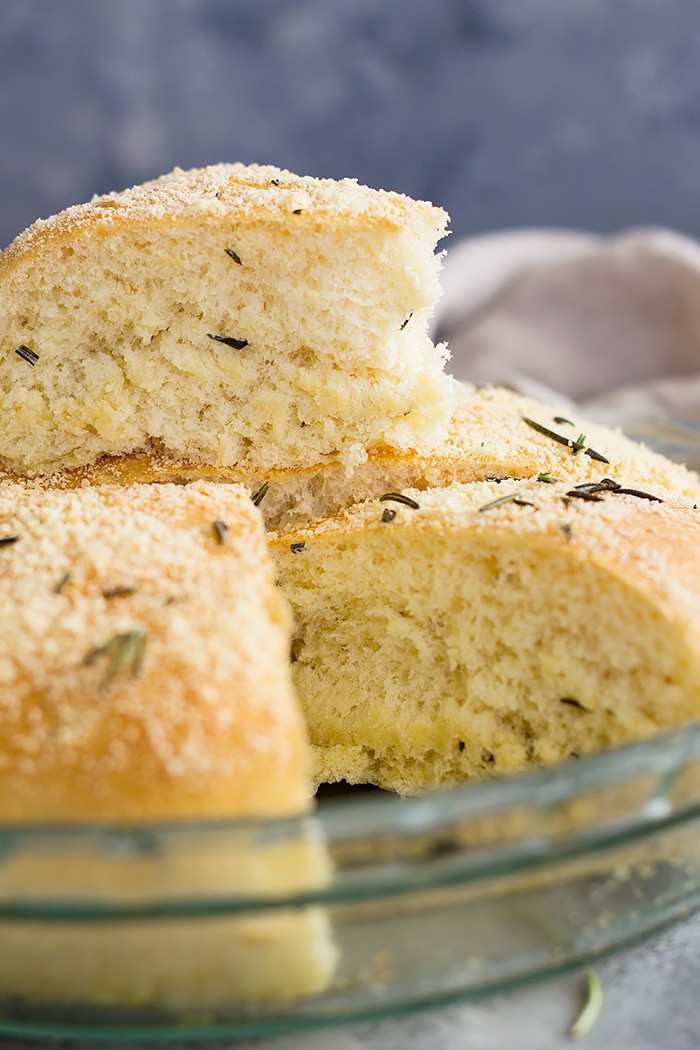 A cut piece of rosemary parmesan bread sitting on top of a round of bread. 