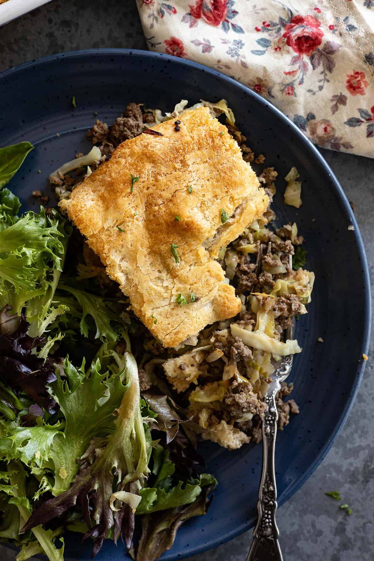 Overhead view of runza casserole with bite taken out showing the contents of the casserole. Salad off to the side of the plate.