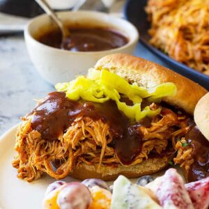 Close up picture of slow cooker bbq chicken on a bun with bbq sauce.