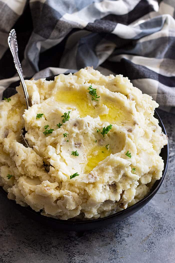 Large bowl of slow cooker mashed potatoes topped with butter and chopped parsley to garnish.
