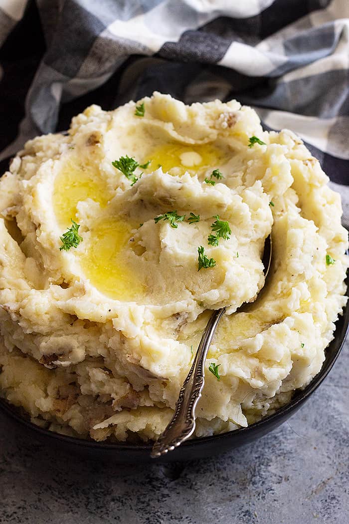 Large bowl of slow cooker mashed potatoes topped with butter and chopped parsley to garnish. 