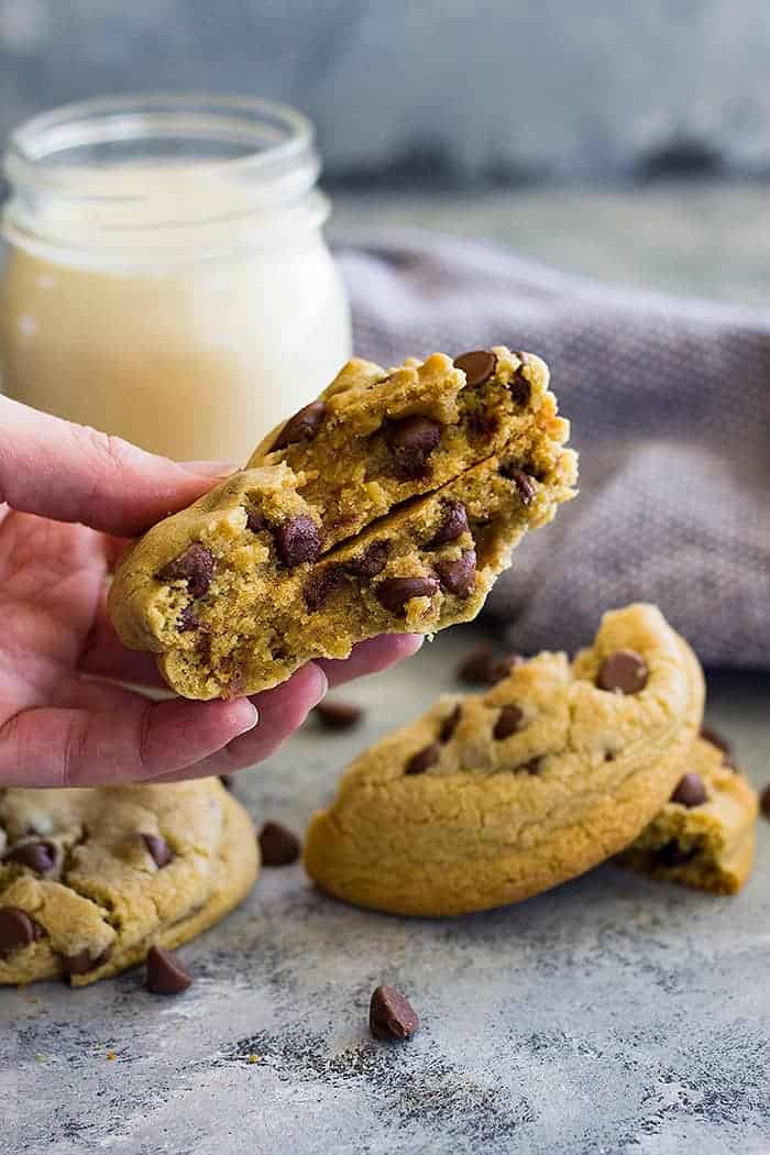 A hand holding two halves of a cookie for two showing the center. Milk and cookies in the background. 
