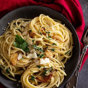Top down view of spaghetti in a dark bowl and garnished with parmesan and parsley.