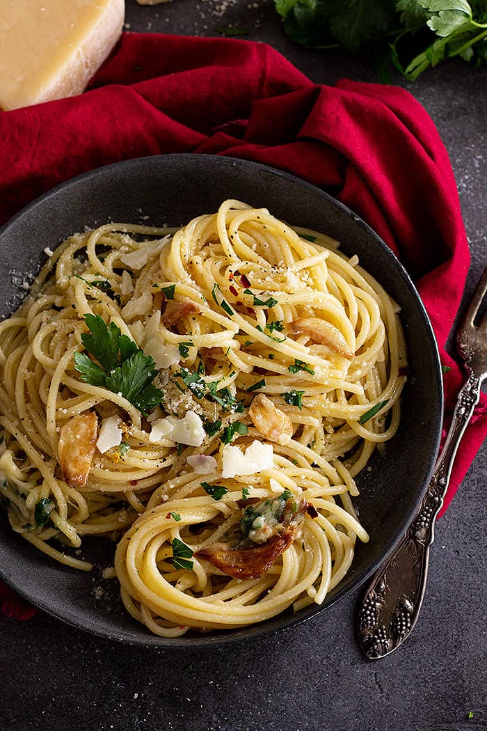 Top down view of spaghetti in a dark bowl and garnished with parmesan and parsley.