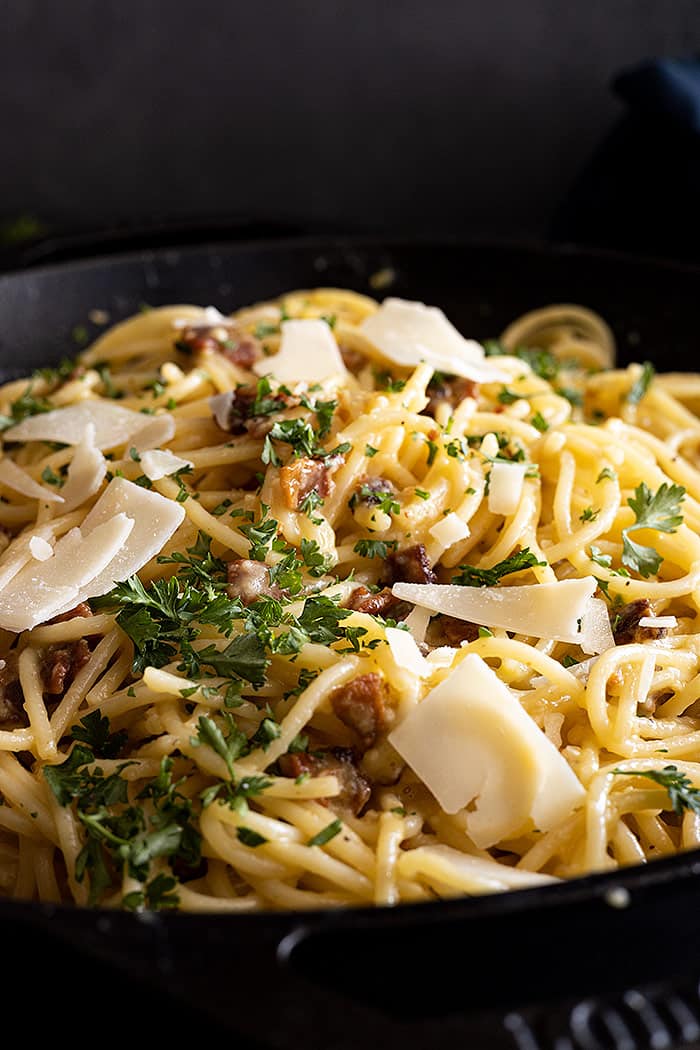 Close up of carbonara garnished with pieces of shaved parmesan and parsley.