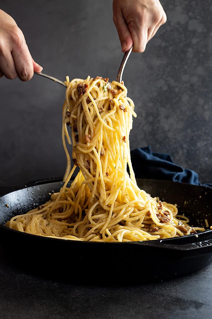 Two forks pulling up a generous portion of spaghetti carbonara ready to serve. 
