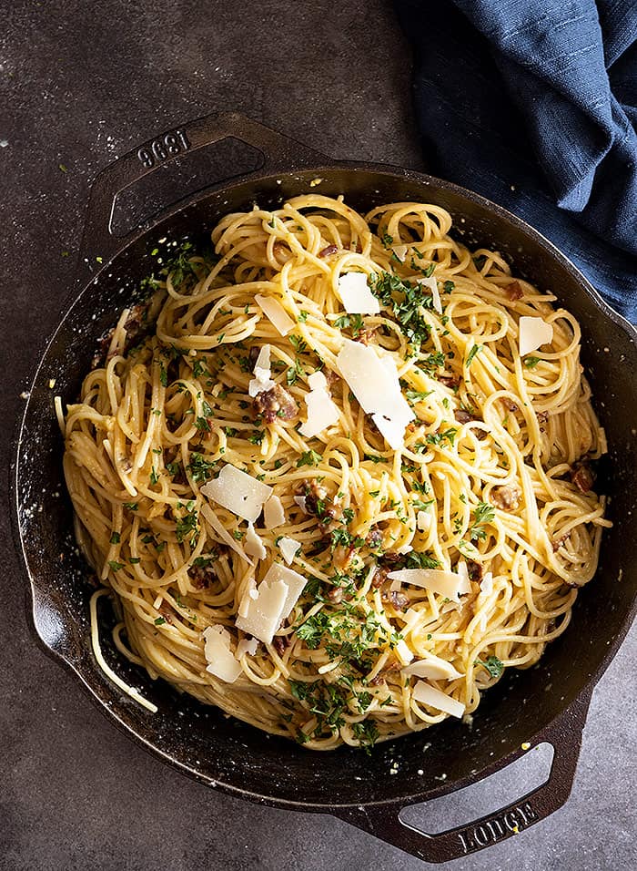 Overhead view of carbonara in a cast iron skillet garnished with parmesan and parsley. 
