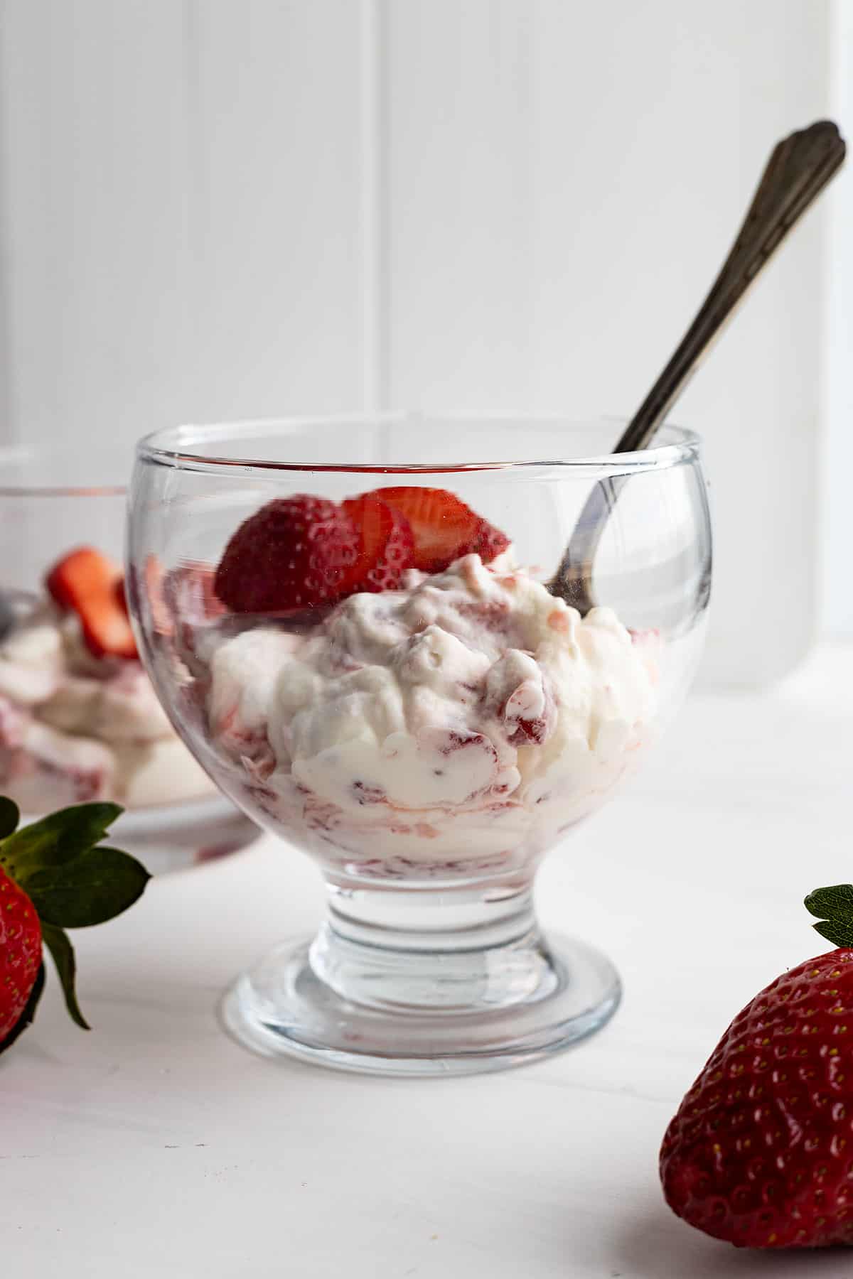 A cup of fool with a spoon sticking out and garnished with strawberries. 