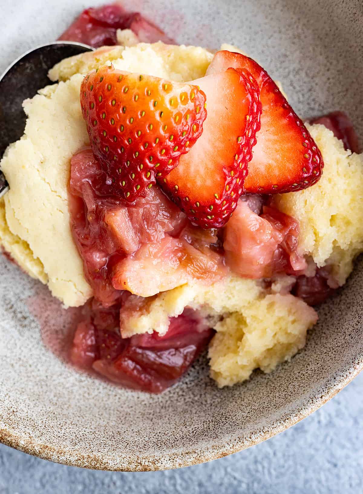 Overhead view of strawberry rhubarb pudding cake in a bowl. Fresh strawberries on top.