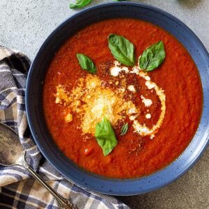 Top down view of a bowl of soup garnished with fresh basil, cream, cheese, and black pepper.