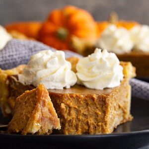 Close up of a slice of traditional pumpkin pie with a bite taken out to show how smooth and creamy it is.