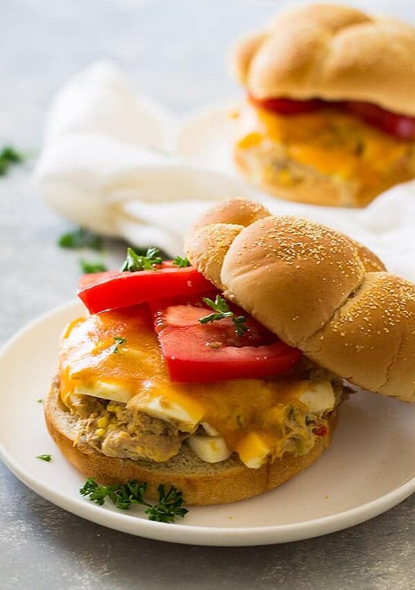 Close up shot of sandwich with hamburger bun, sliced tomato, and cheese on white plate.