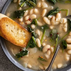 Close up of soup in a bowl. Piece of crusty garlic bread dunking into the soup.