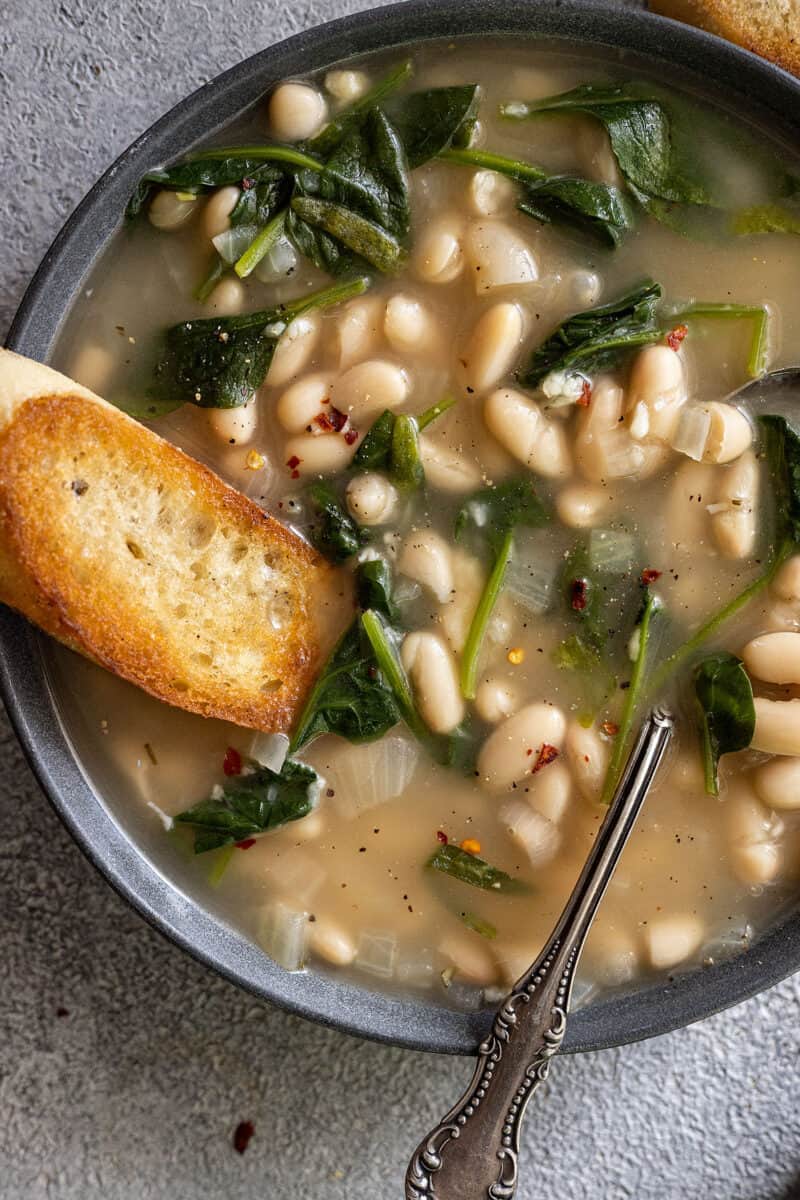 Close up of soup in a bowl. Piece of crusty garlic bread dunking into the soup.